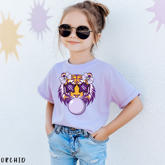 Child wearing a purple t-shirt with a tiger design, sunglasses, and ripped jeans against a light background.