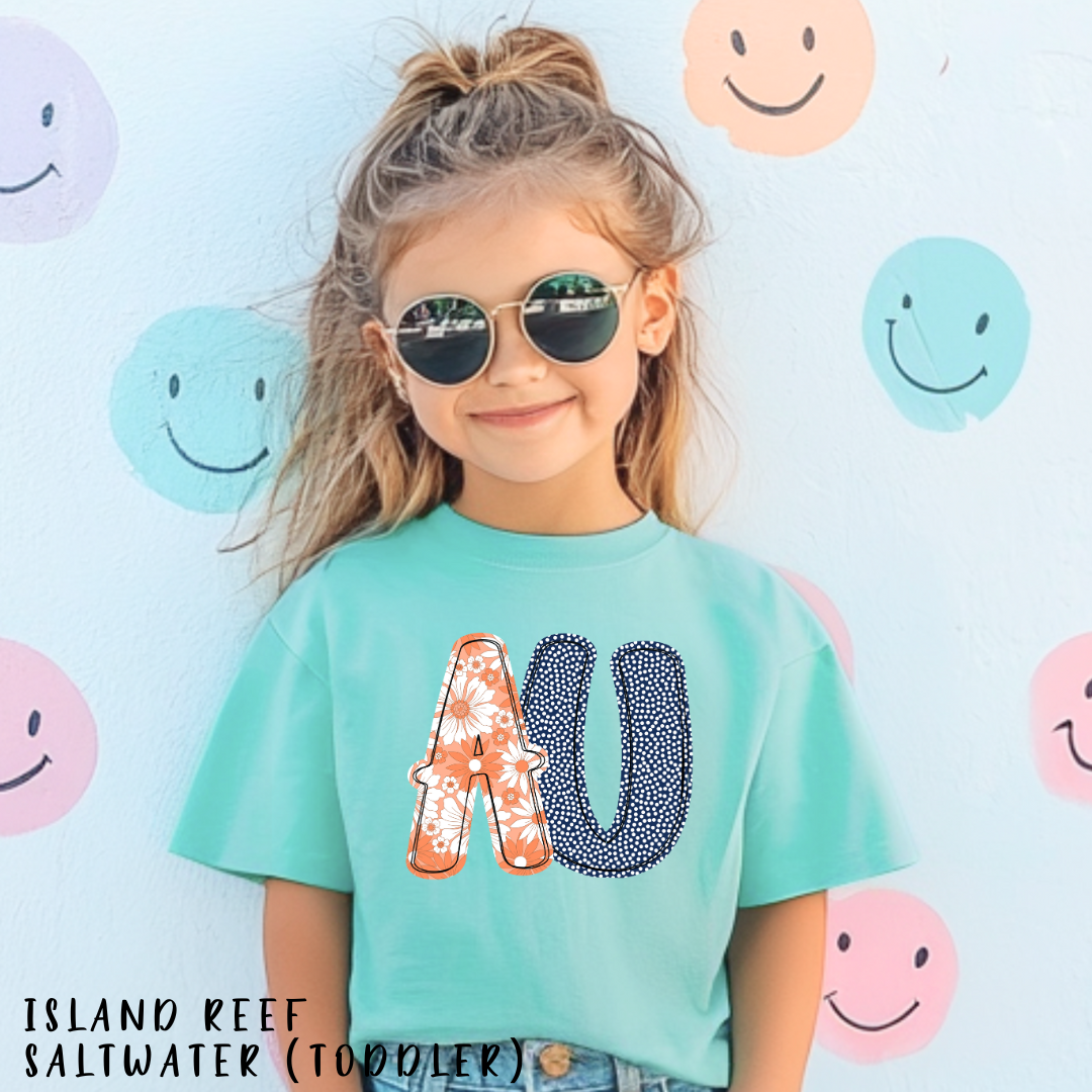 Child wearing a teal t-shirt with colorful letters against a background of smiley faces.