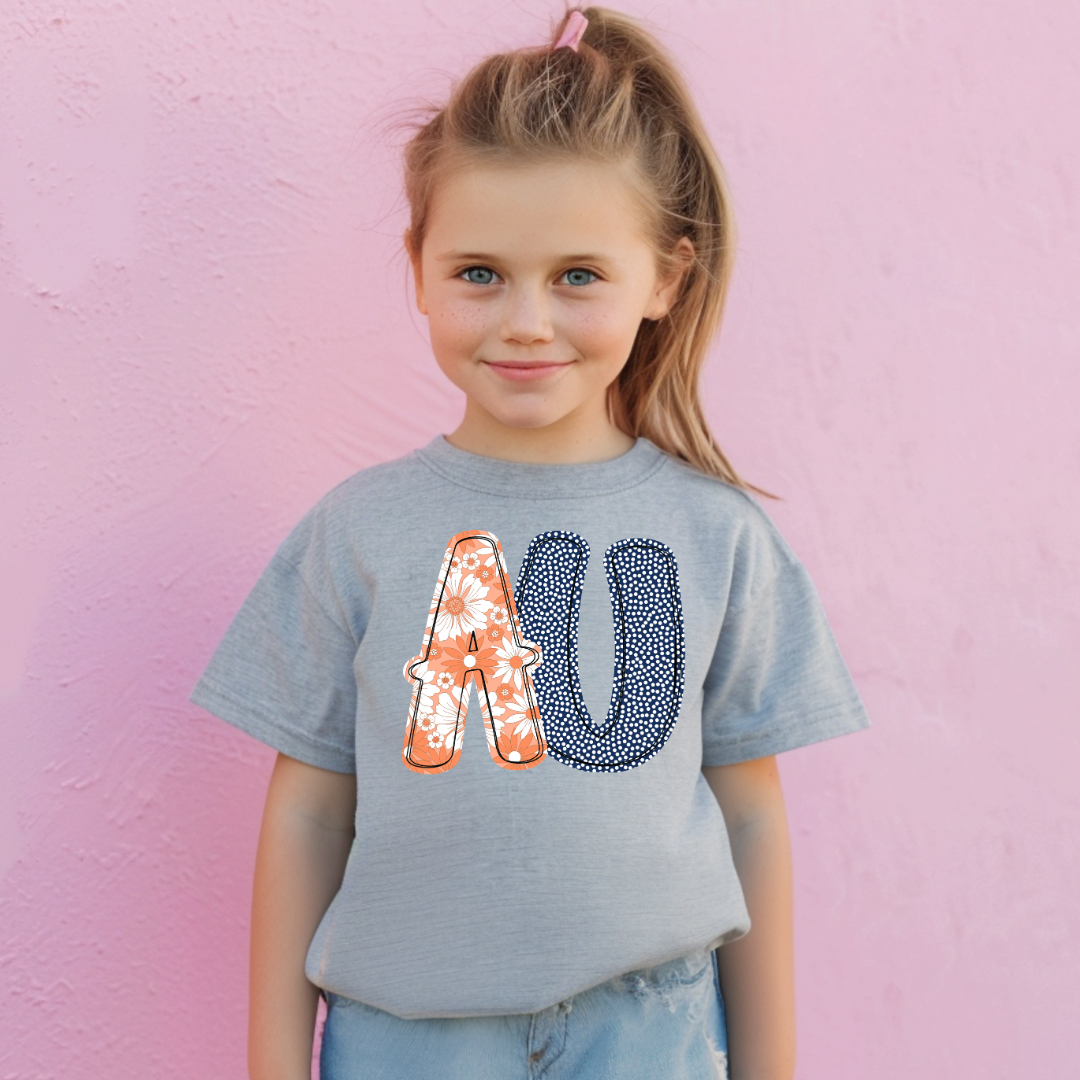Young girl wearing a gray t-shirt with decorative letters 'AU' against a pink background