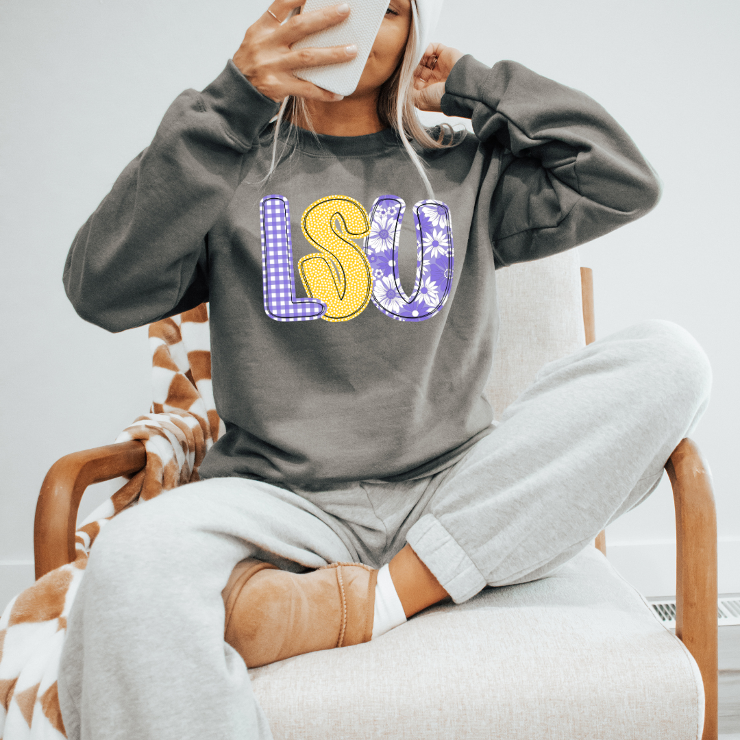 Person wearing a gray sweatshirt with 'LSU' printed on it, sitting on a chair.
