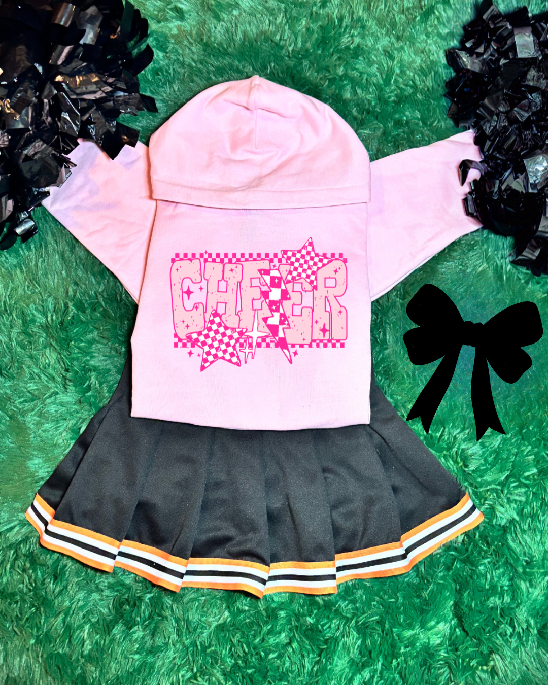 Pink hoodie with 'CHEER' design, black skirt, and pom-poms on a green grass background