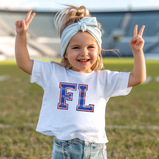 Child wearing a white t-shirt with 'FL' on it, standing outdoors.