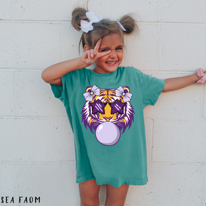 Child wearing a teal t-shirt with a tiger graphic design, standing against a white brick wall.