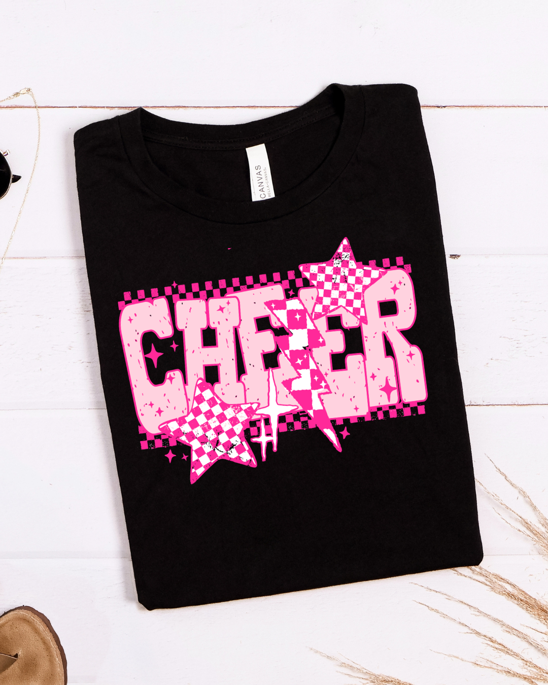 Black t-shirt with pink 'CHEER' design on a white wooden surface