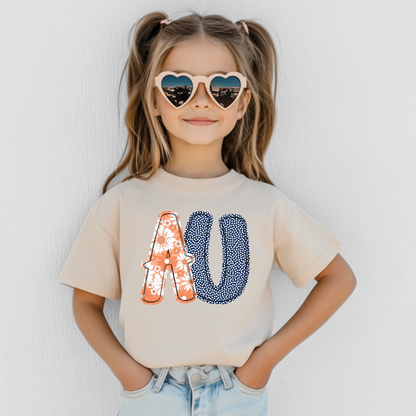 Child wearing a beige t-shirt with colorful letter design, heart-shaped sunglasses, and light blue jeans against a white background.