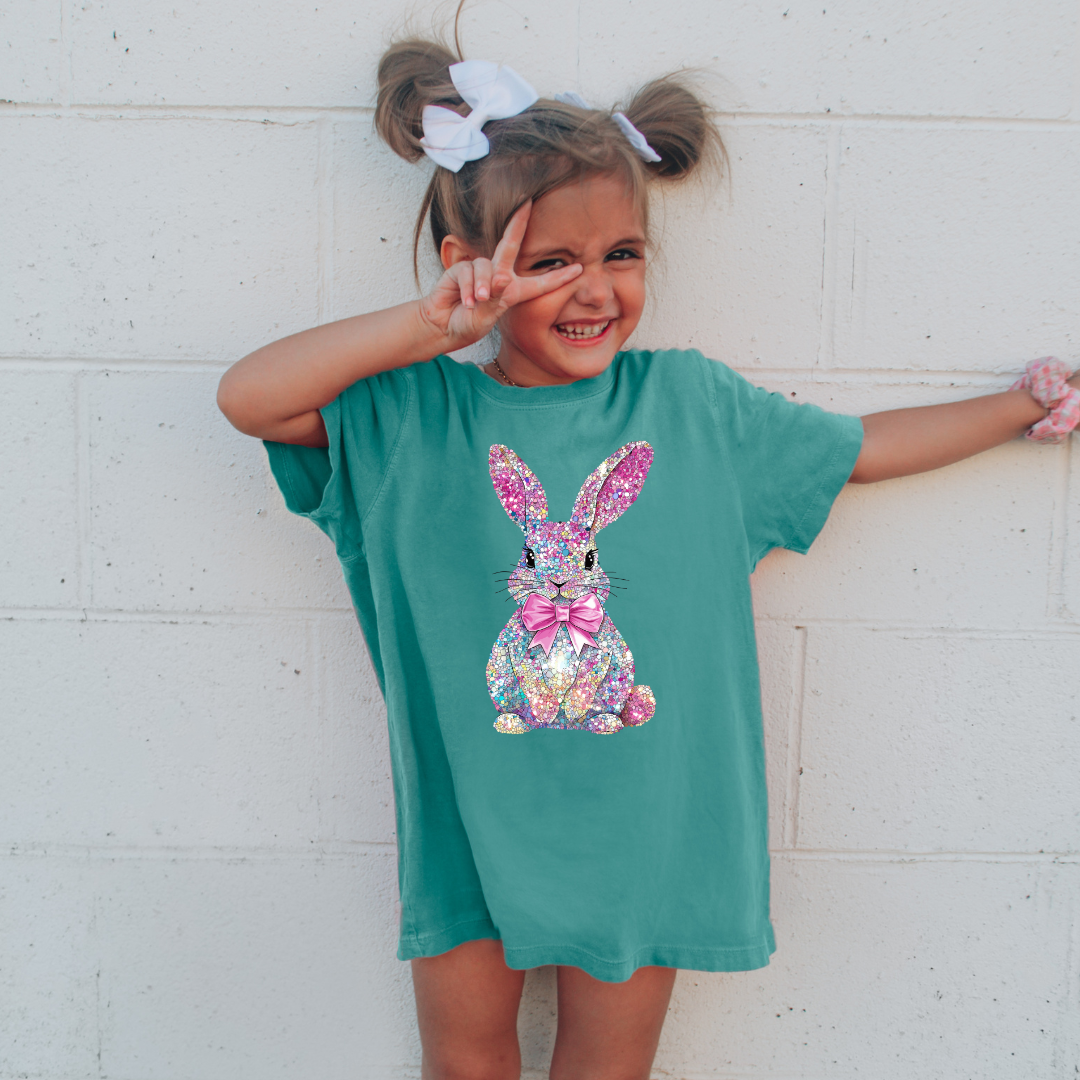Child wearing a teal t-shirt with a colorful bunny design against a white wall.