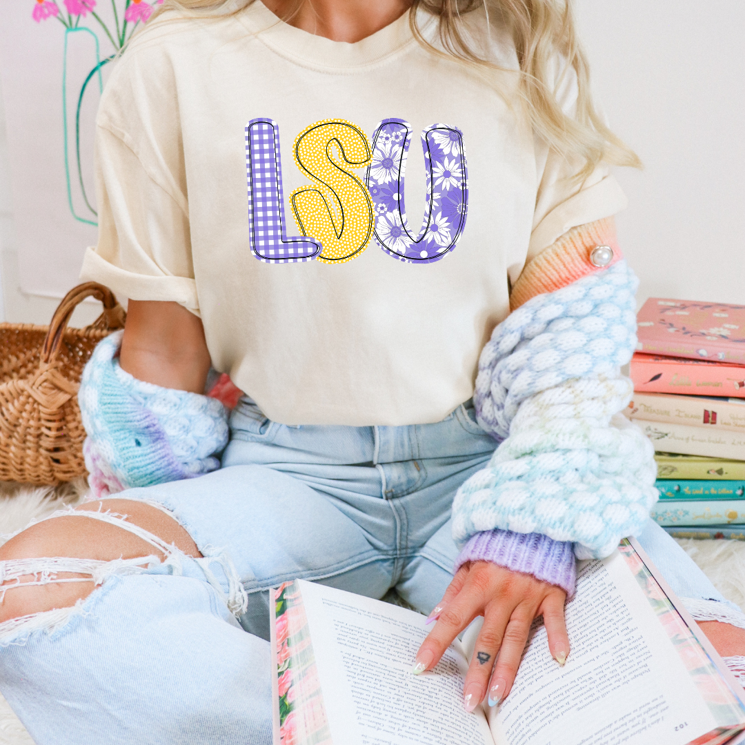 Person wearing a cream sweatshirt with 'LSU' printed on it, sitting on books.