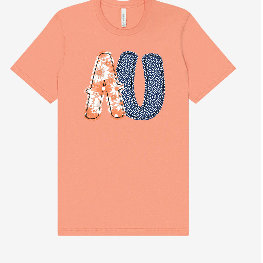 Peach-colored t-shirt with floral and polka dot letters 'AU' on a white background