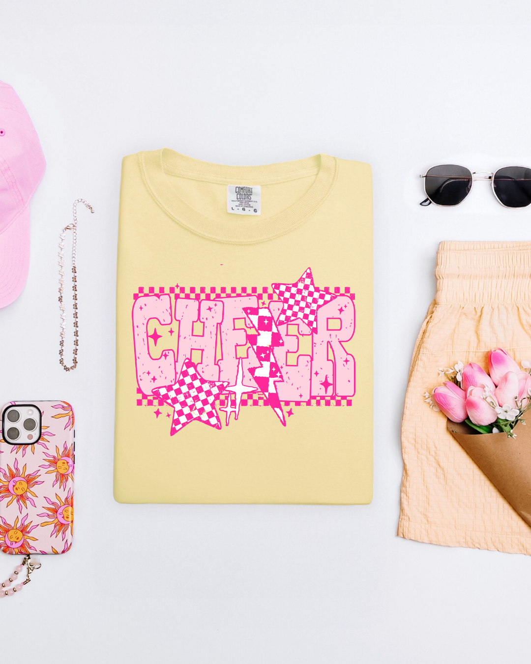 Yellow t-shirt with pink 'CHEER' design on a white surface with accessories.